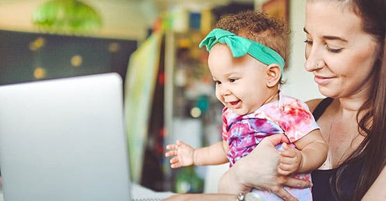 Woman holding her baby looking at a computer screen